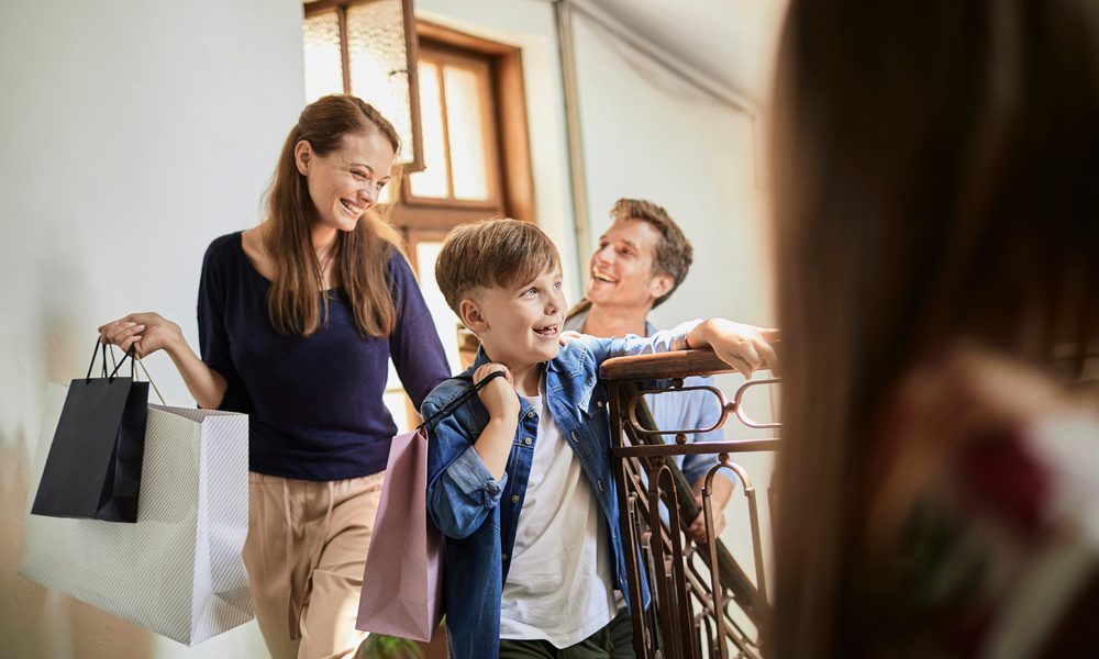 A family of four walking through a bright doorway with shopping bags, coming home after a holiday vacation.