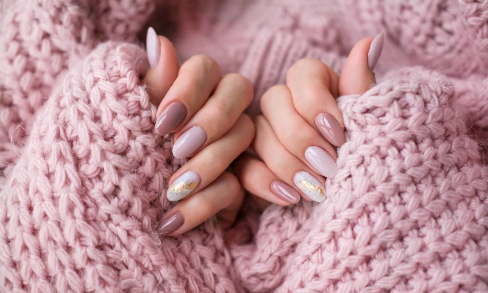 A close-up view shows a woman's hands curled toward her palms to show her painted nails. She's wearing a pink sweater.